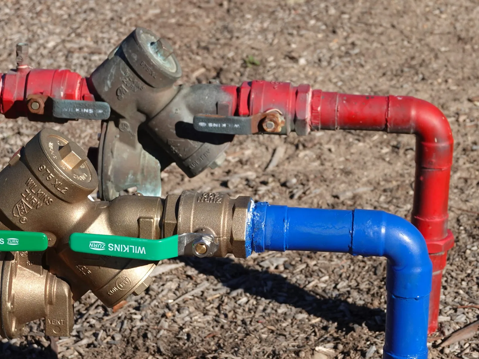 Old and new backflow preventers side by side on painted pipe, backflow prevention