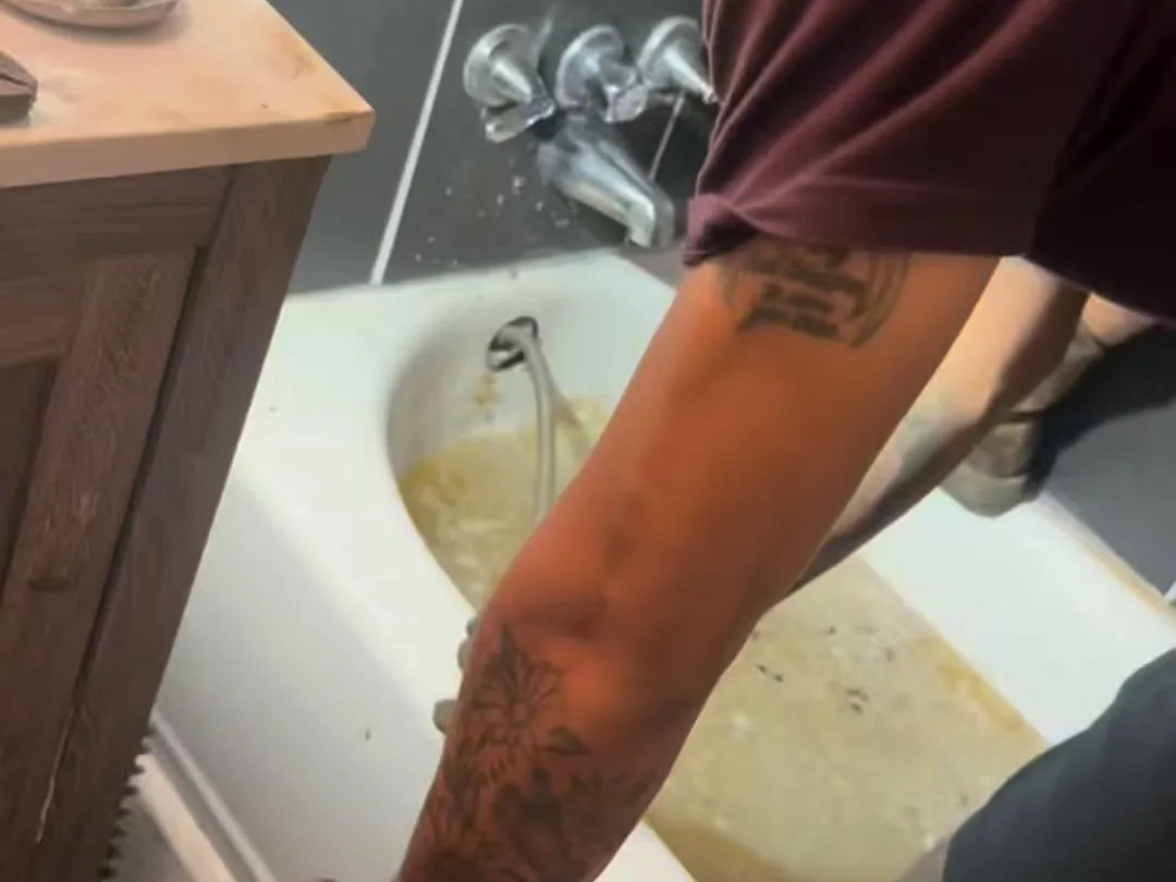 Plumber running a drain snake into a clogged bathtub drain, drain cleaning