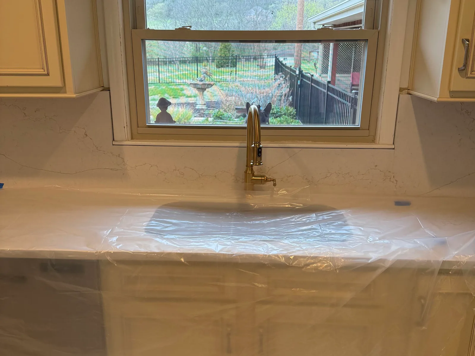 New brass kitchen faucet at a sink under a window, faucet repair and installation