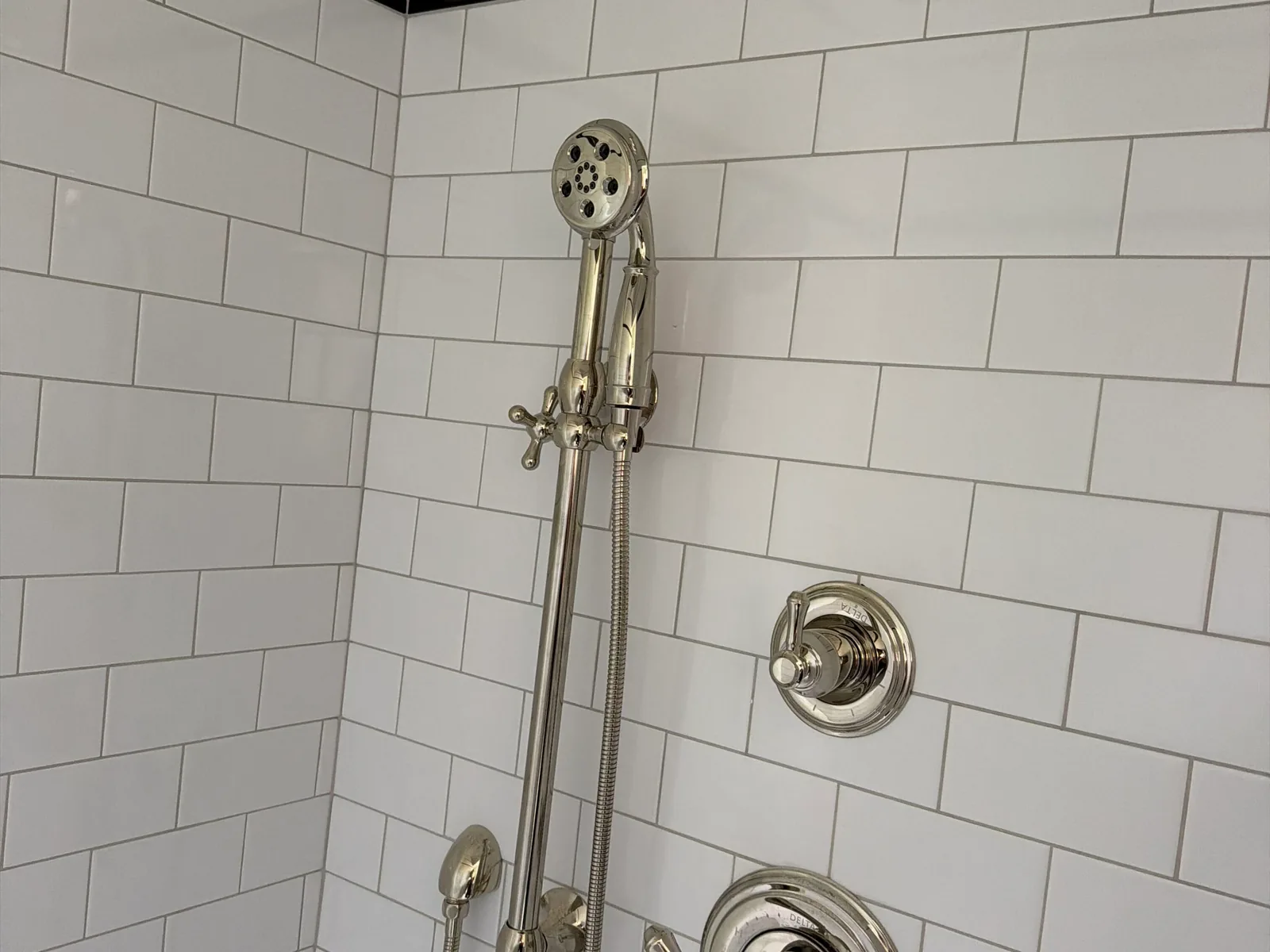 Polished nickel shower valve trim and handheld shower on subway tile, faucet repair