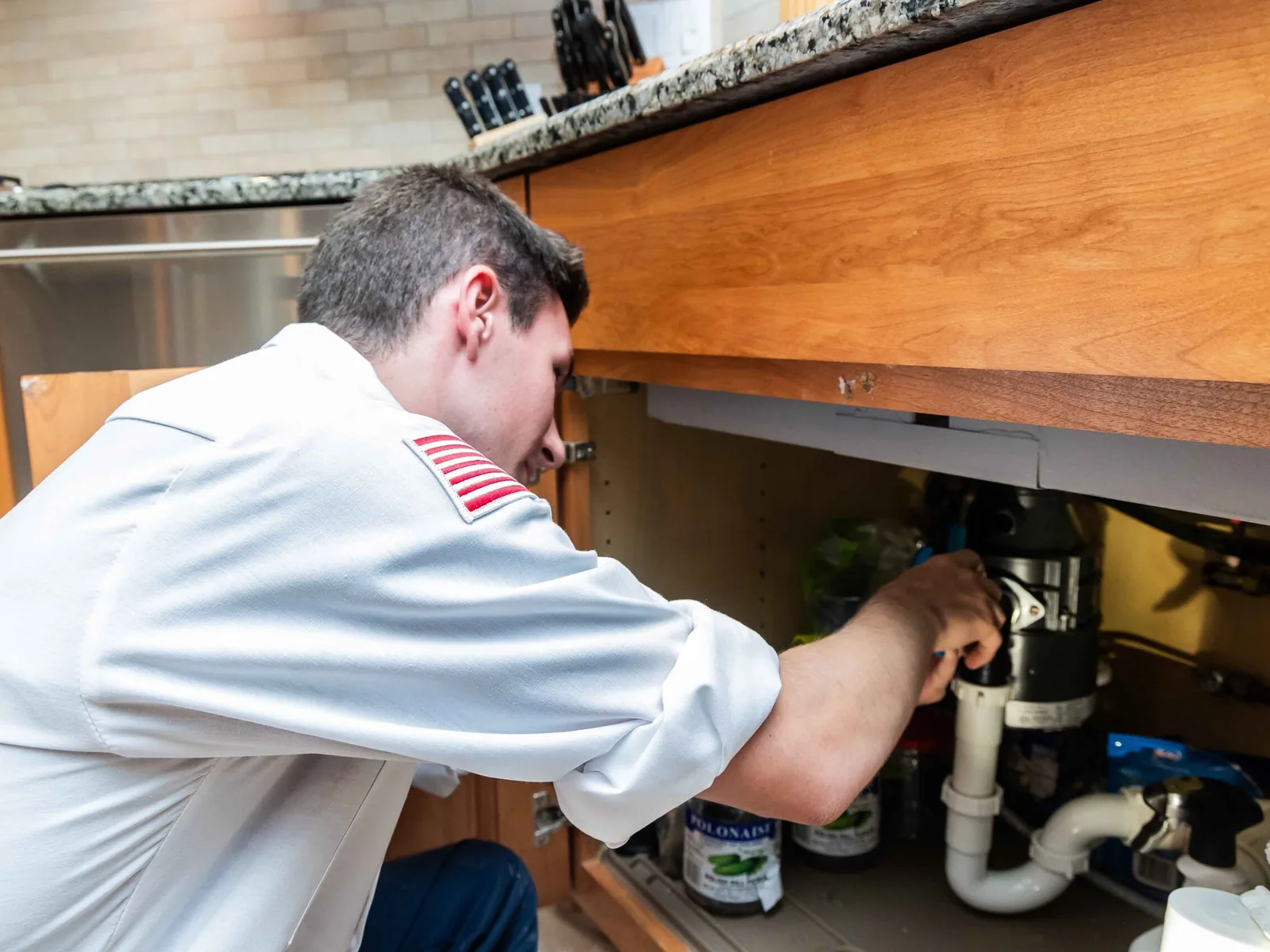 Technician working on a garbage disposal under a kitchen sink, garbage disposal repair