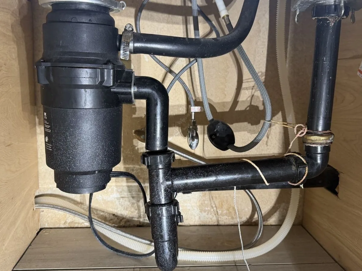 Garbage disposal with black drain pipes under a kitchen sink, garbage disposal repair