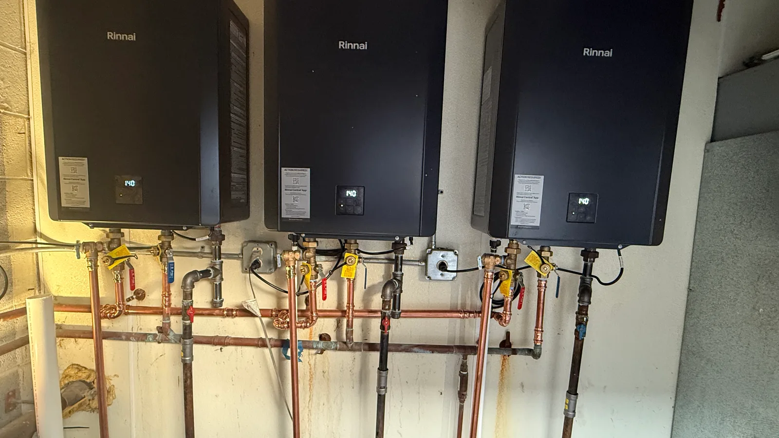 Plumber installation of three tankless water heaters with copper and gas piping on a wall