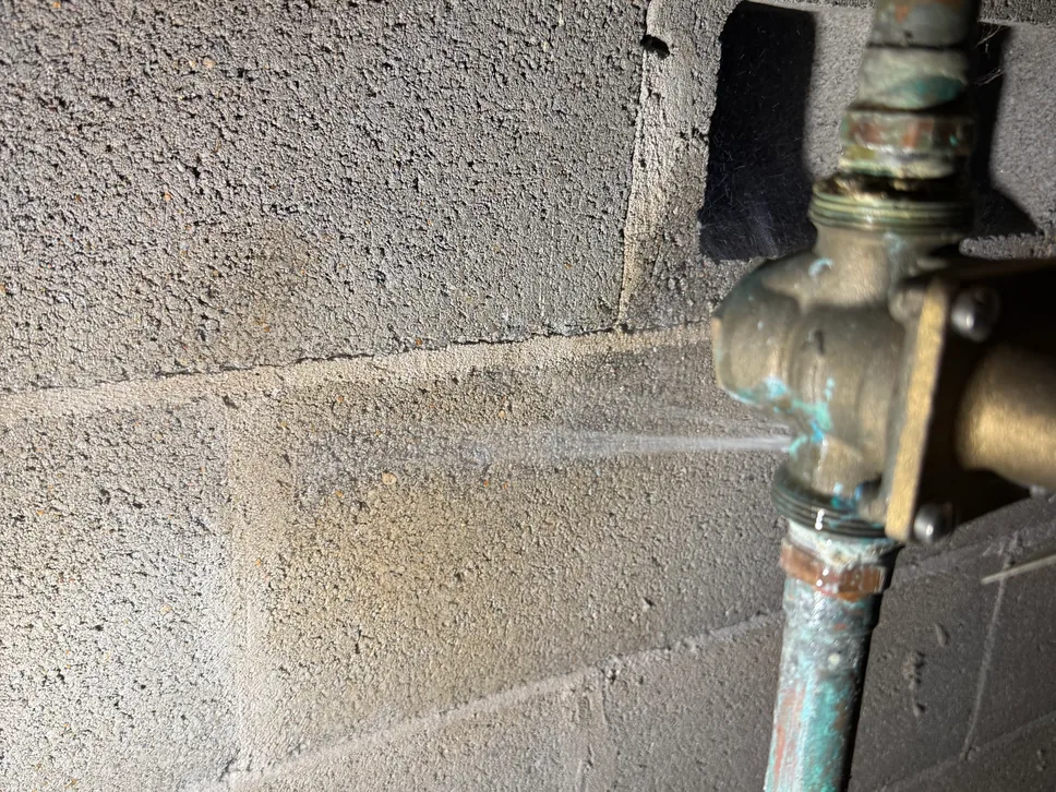 Water spraying from a leaking valve on a copper pipe by a block wall, leak detection