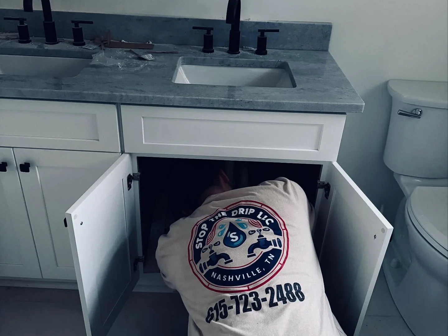 Plumber working on the pipes under a bathroom vanity sink, leak detection