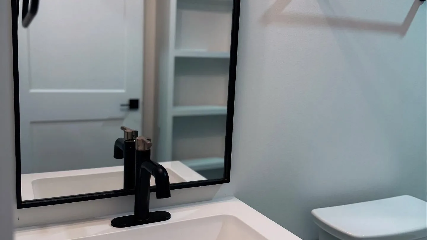 Vanity with a black faucet and arched mirror, plumbing