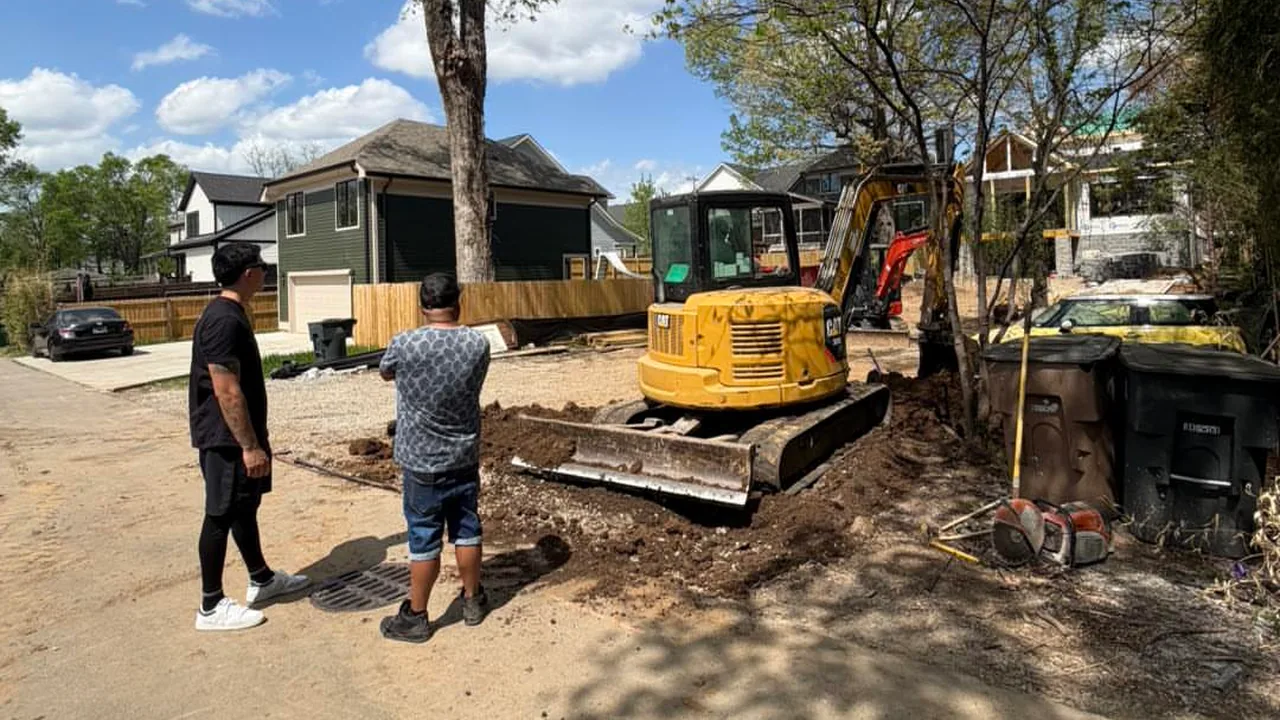 Plumbing crew beside a mini excavator on a residential street
