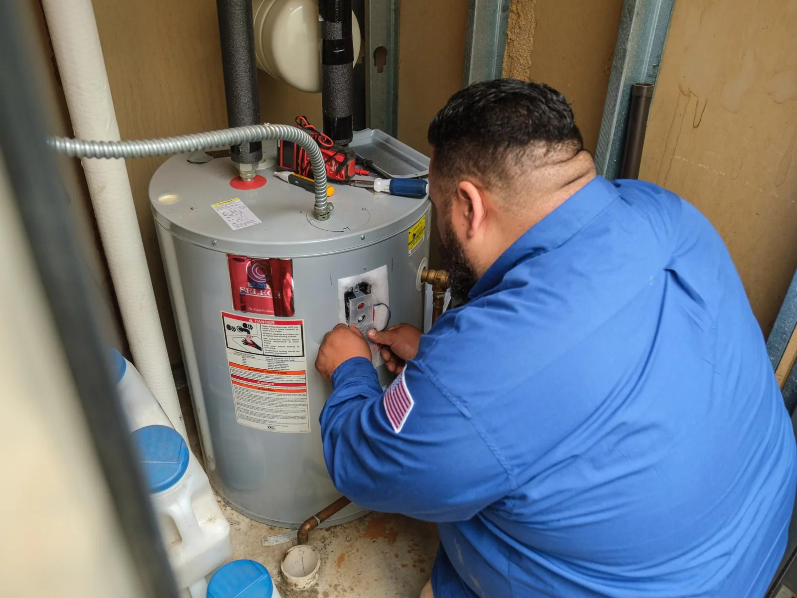Technician working on an electric tank water heater in a utility closet, water heater repair